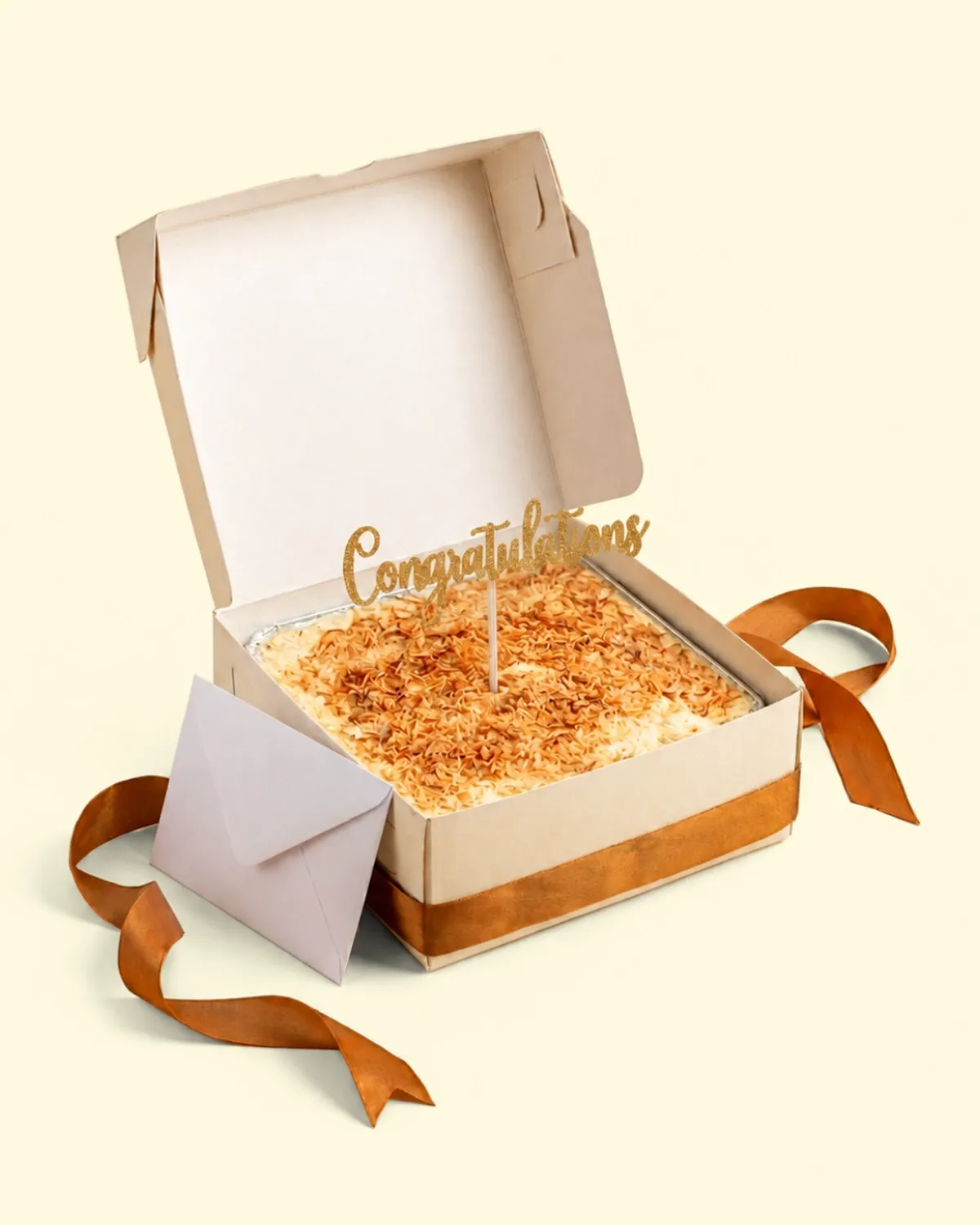 Box hadiah terbuka berisi klappertaart dengan topper, amplop kartu ucapan, dan pita satin