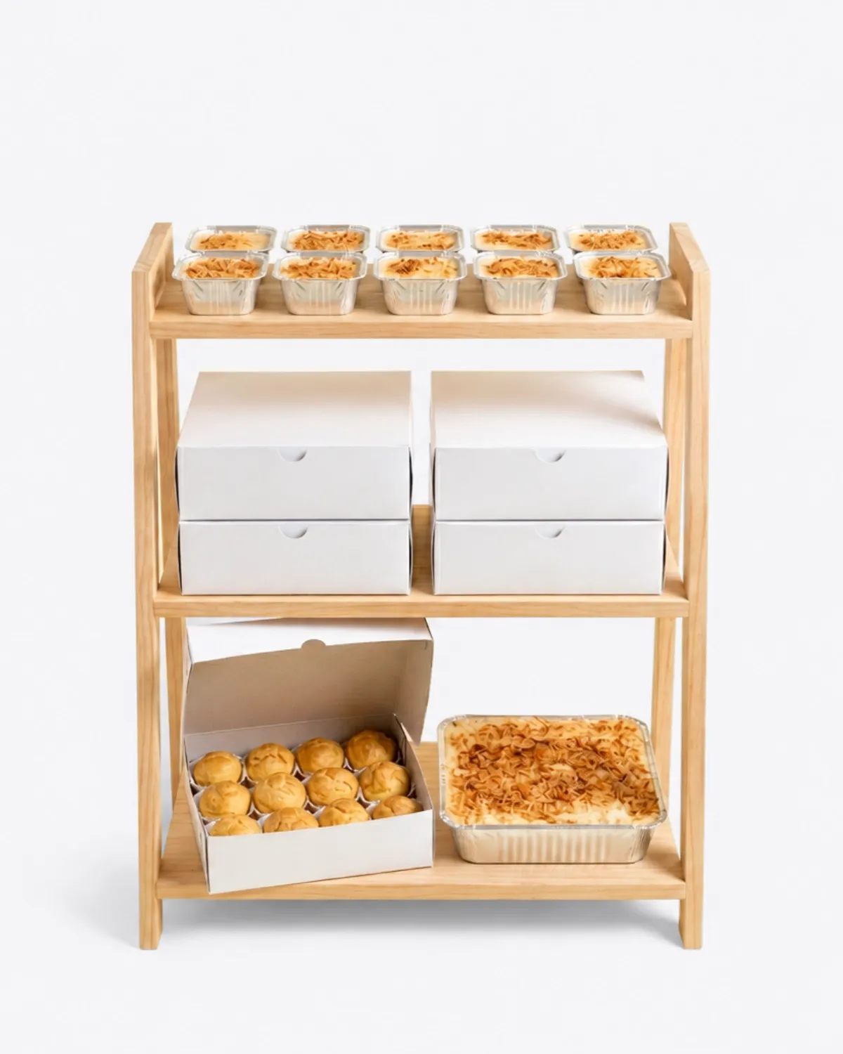 Rak kayu tiga susun berisi klappertaart cup, box putih bertumpuk, satu box soes terbuka, dan satu loyang klappertaart
